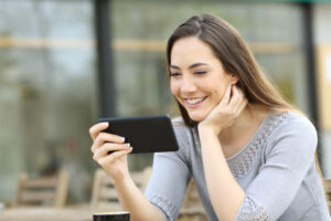 Happy woman watching online video on smart phone in a coffee shop terrace